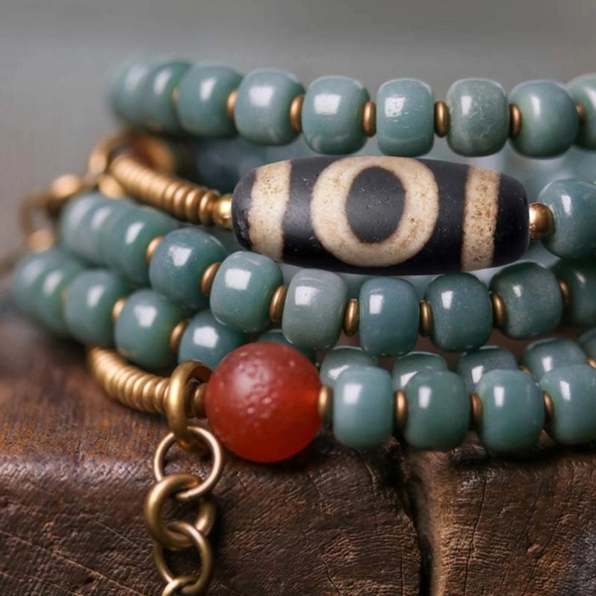 Macro close-up of 108 mala bead set showing detailed dzi bead pattern, red agate bead, teal bodhi seeds, and brass hardware