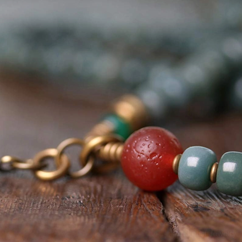 Macro shot of mala bead accessories focusing on metal chains, red agate accents, and teal round bodhi beads