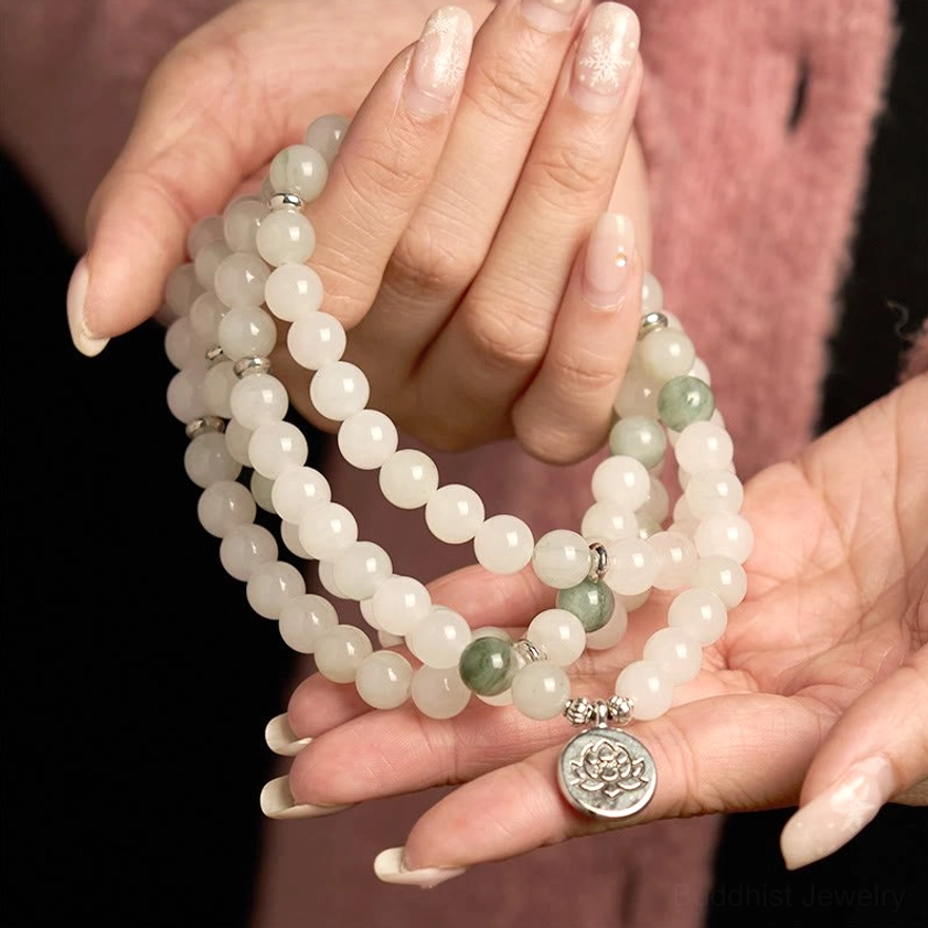 Coiled jade mala beads in hands against pink knitwear, displaying white and green jade stones with silver lotus pendant