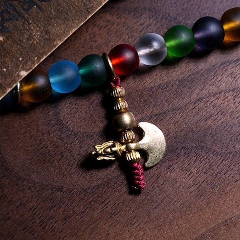 Mala bead bracelet section featuring mixed matte glass beads with vintage metal axe charm and red spiritual tassel accent