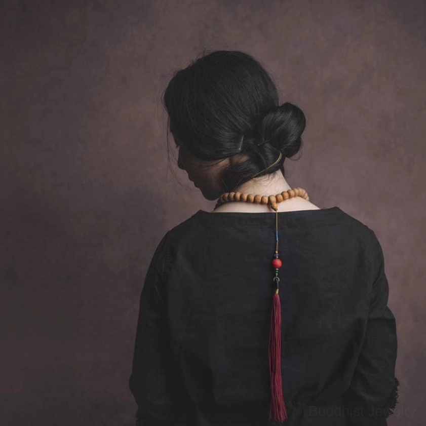 Buddhist mala beads necklace back view worn with black top, showing brown seed beads and red tassel pendant