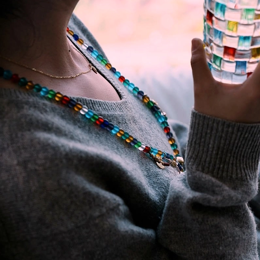 Worn mala bead necklace featuring multicolored frosted glass beads layered with thin chain, lifestyle indoor close-up wear view