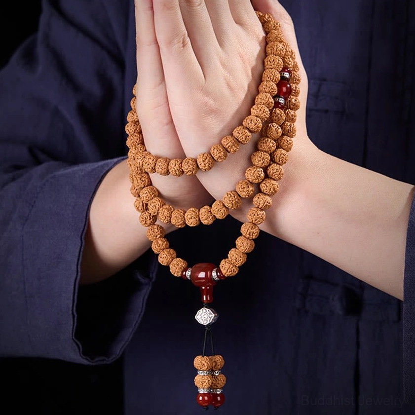 Two hands holding 108 bead Buddhist mala with three-eye dzi and tassel pendant detail shot