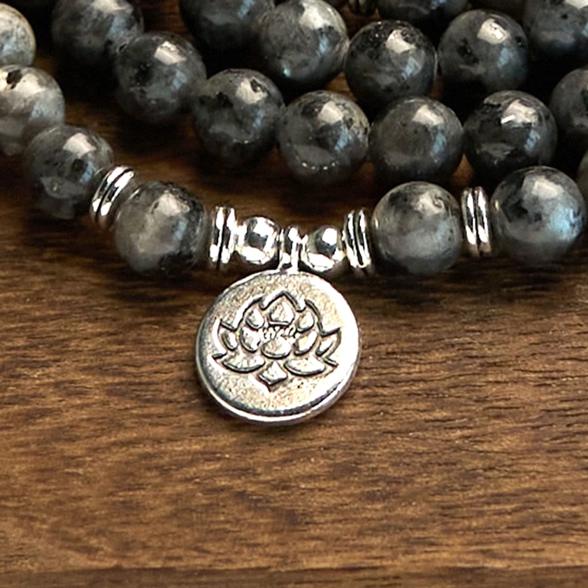 Extreme close-up detail of textured black glitter stone mala beads and engraved lotus charm