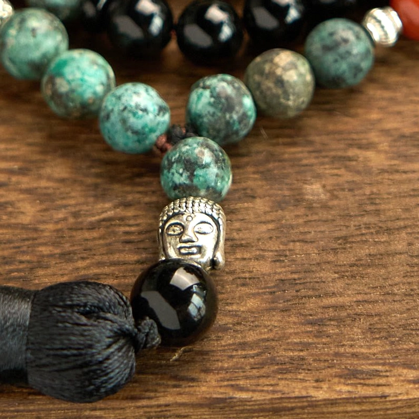 Detailed macro view of Buddhist mala bracelet featuring silver Buddha head charm, black silk tassel, and polished natural gemstone beads