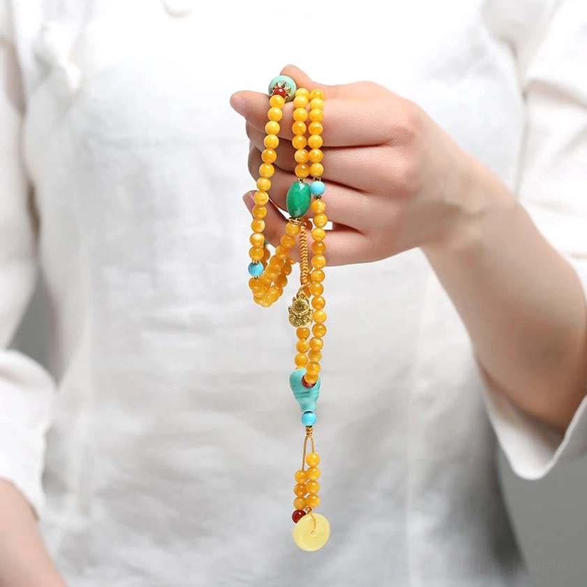 Close-up detail of multi-layered amber mala bracelet with hand-strung beads, tasseled pendant and gemstone decorations
