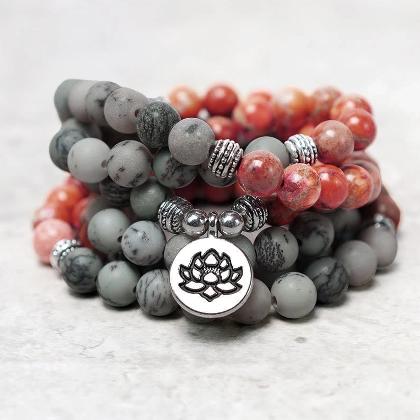 Close-up side view of stacked mala bead bracelets showing red and gray jasper beads with large lotus charm