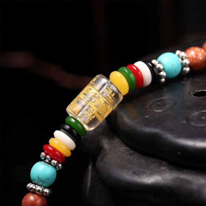 Macro close-up of mala bead components showing transparent mantra barrel bead, colorful ring spacers, and turquoise accents