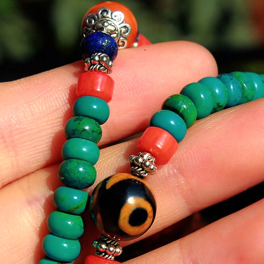 Close-up detail of dzi bead and turquoise stone in Buddhist 108-bead mala bracelet