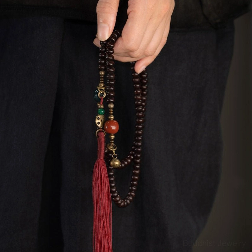 Hand-held 108 Mala Prayer Bracelet with dark brown bodhi seeds, red tassel, and decorative ornaments against clothing
