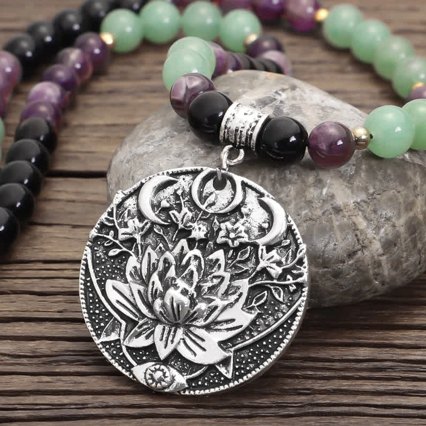 close-up detailed view of mala bracelet with intricately engraved silver lotus charm, amethyst and green aventurine beads on river stone