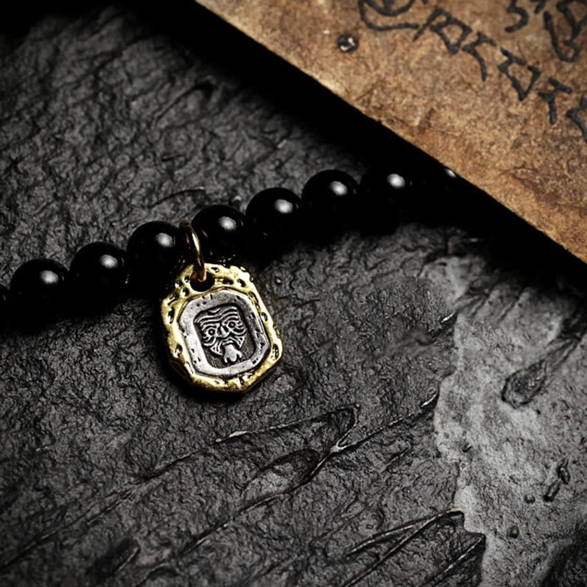 Buddhist mala bracelet with protective brass face charm on dark stone with vintage scripture
