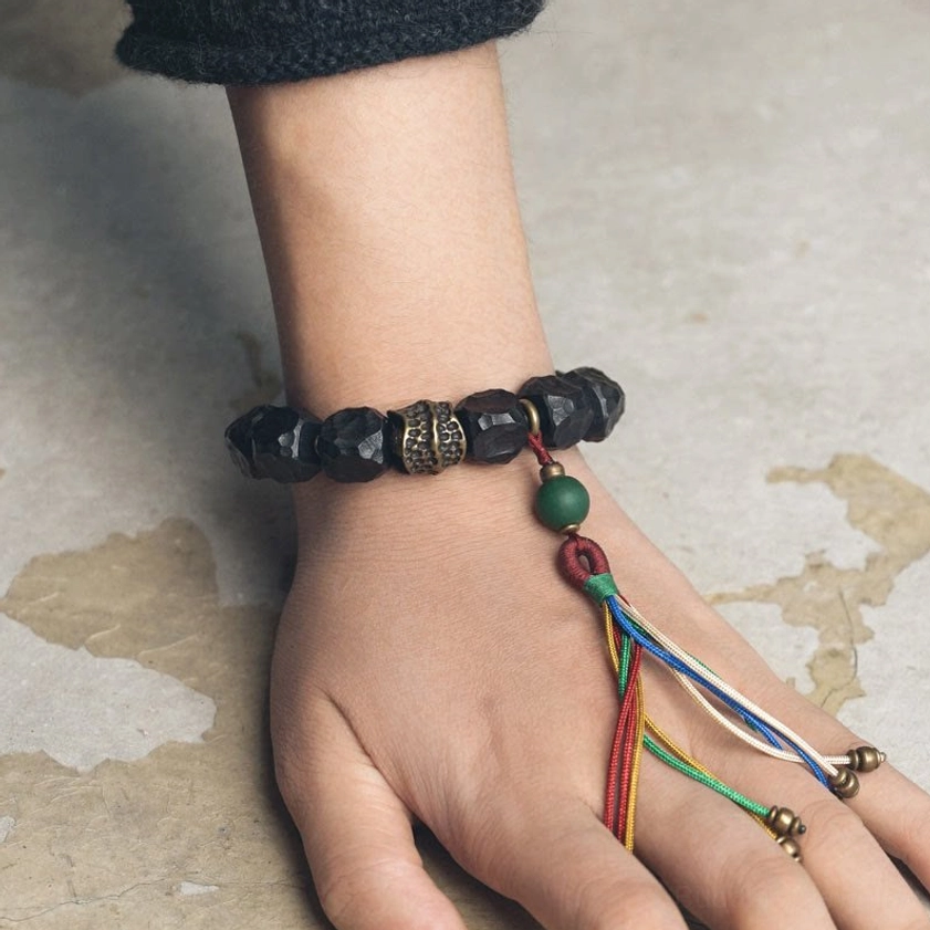 Hand holding Buddhist prayer mala bracelet showing green accent bead and multicolor tassel