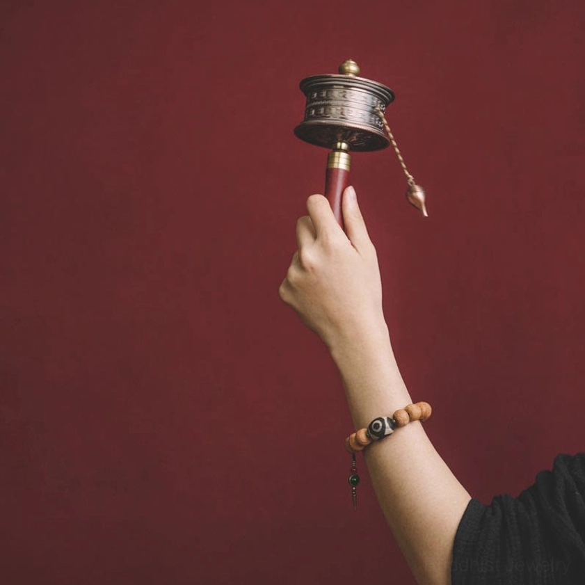 Hand holding prayer wheel with bodhi seed mala bracelet on arm