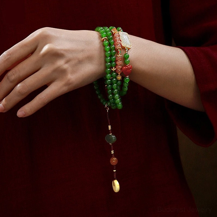 Woman wearing jade and red agate mala bracelet with tassel on wrist against red fabric background