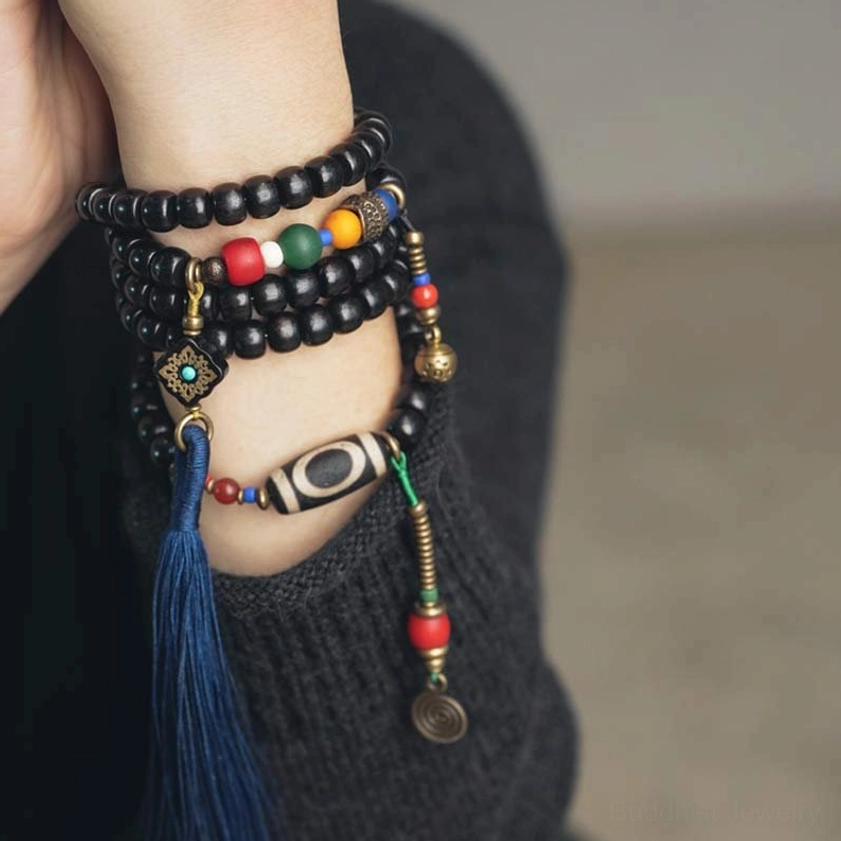 Layered mala bracelets on wrist showing 108 beads, dzi bead, and blue tassel detail