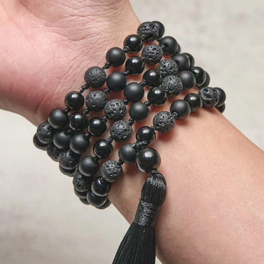 Black beaded mala bracelet wrapped around wrist, close-up side view showing textured gemstone beads with charm