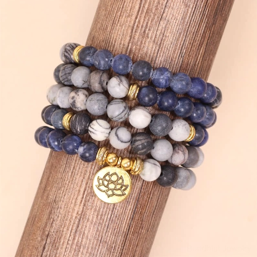 Stacked mala bracelets displayed on wooden holder showing sodalite zebra jasper stones and gold lotus charm close-up