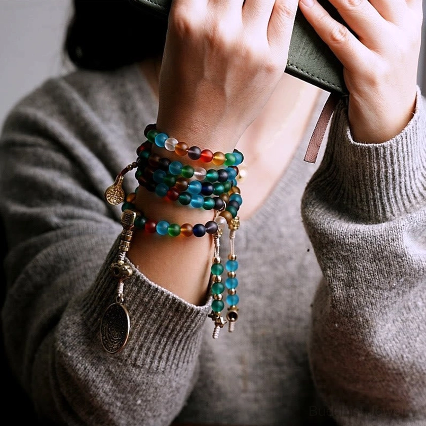 Stacked mala bead bracelets on wrist showing multiple colorful strands with metal pendants, indoor daily wear lifestyle shot