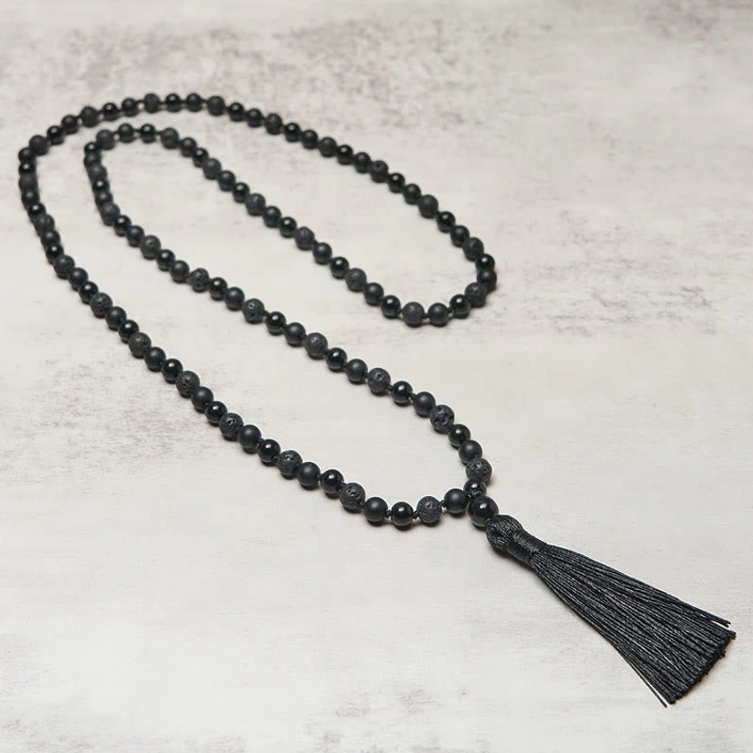 Long beaded tassel mala necklace displaying uniform black stones, flat lay against neutral background