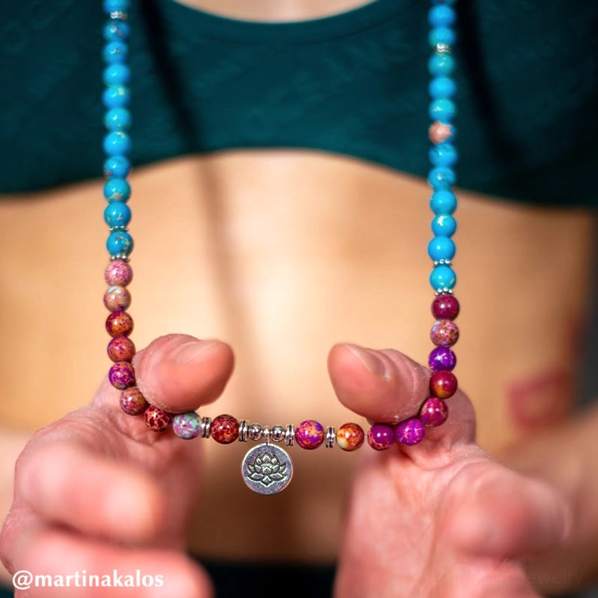 Purple and red accent beaded mala necklace held close to chest with teal top - authentic Buddhist meditation jewelry