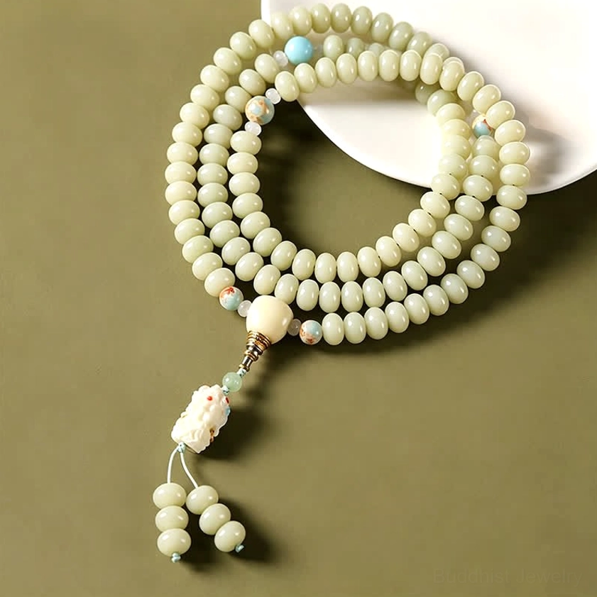 White bodhi seed Buddhist prayer mala with blue accent beads and Tara pendant shown on white ceramic plate