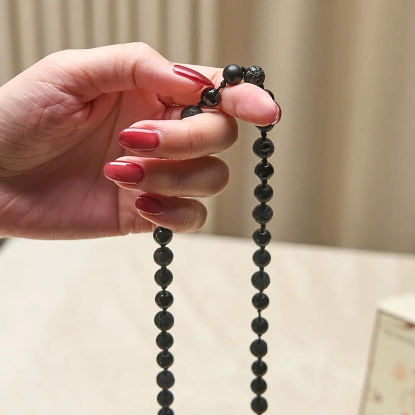Hand-held Buddhist mala necklace with round black gemstone beads, detail view of bead spacing and tassel