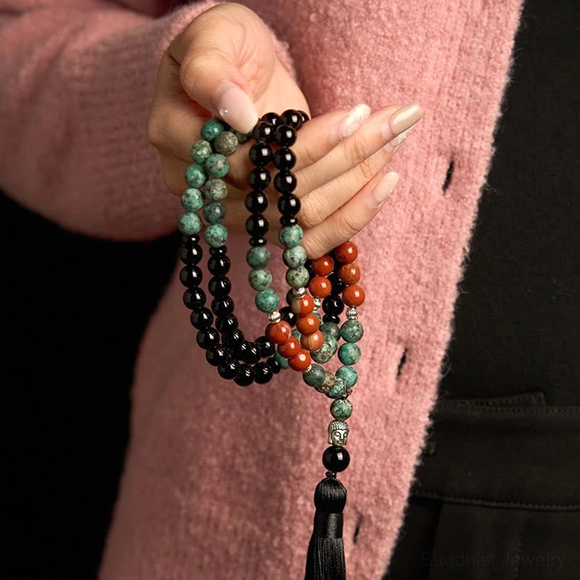 Single hand holding 108-bead mala bracelet showing neatly arranged gemstone beads in black onyx, turquoise, and red jasper with black tassel