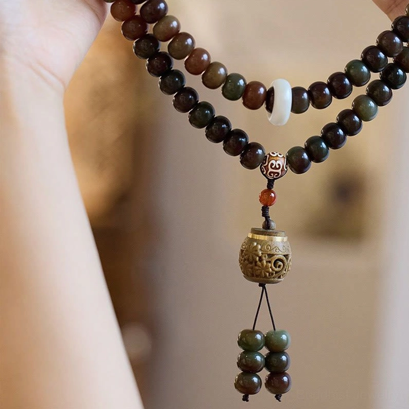 Multi-strand mala prayer beads bracelet worn on arm, showing layered Bodhi seed beads with white spacer and carved pendant detail