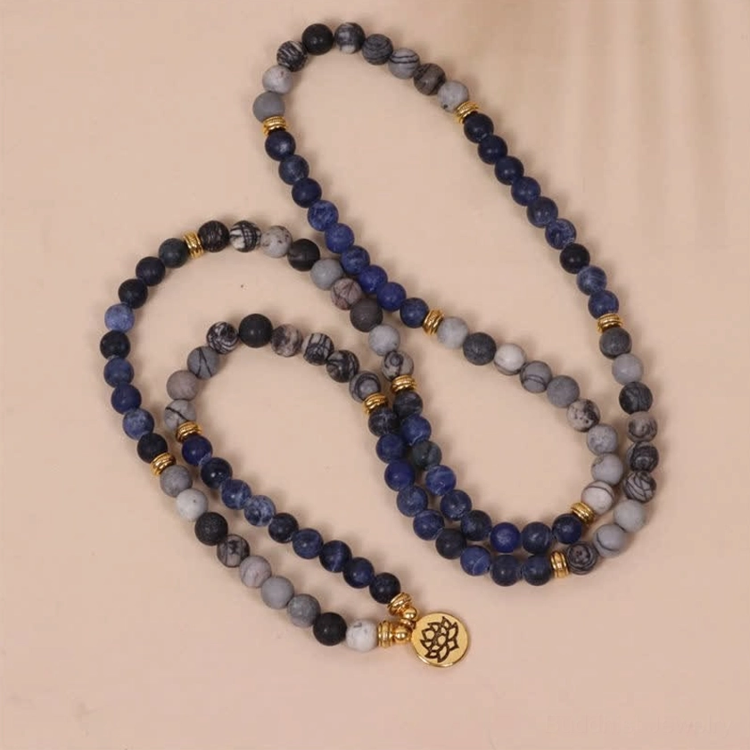 Long mala bead strand with blue-grey stone beads gold spacers and lotus charm on pale pink background