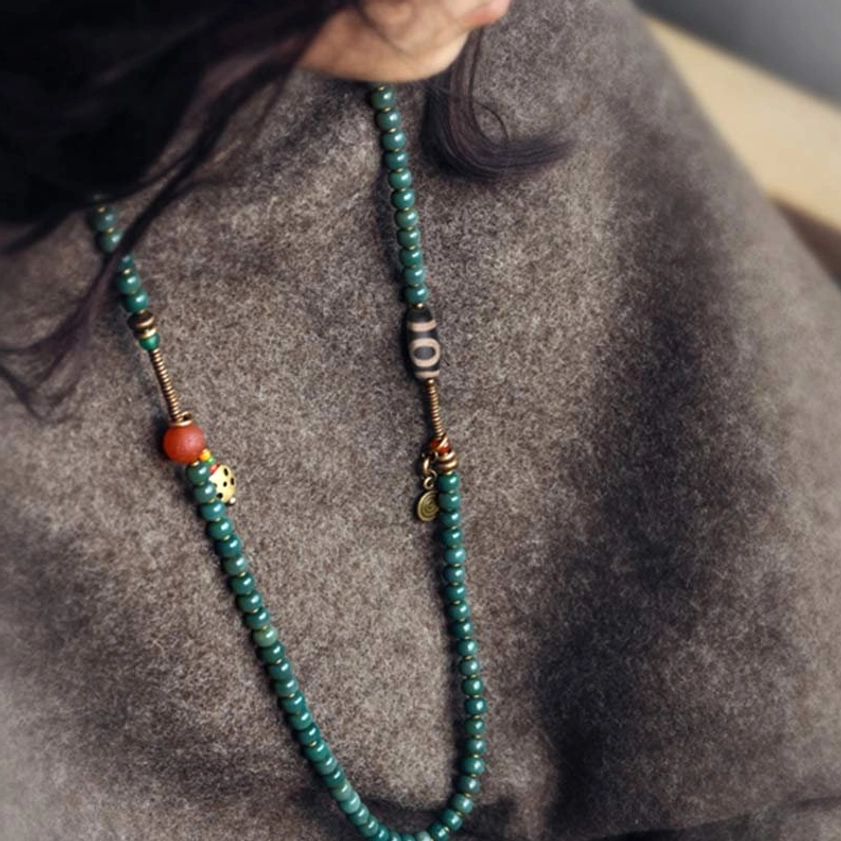 Double-strand Buddhist prayer mala necklace with dzi bead and hanging metal trinkets over grey clothing