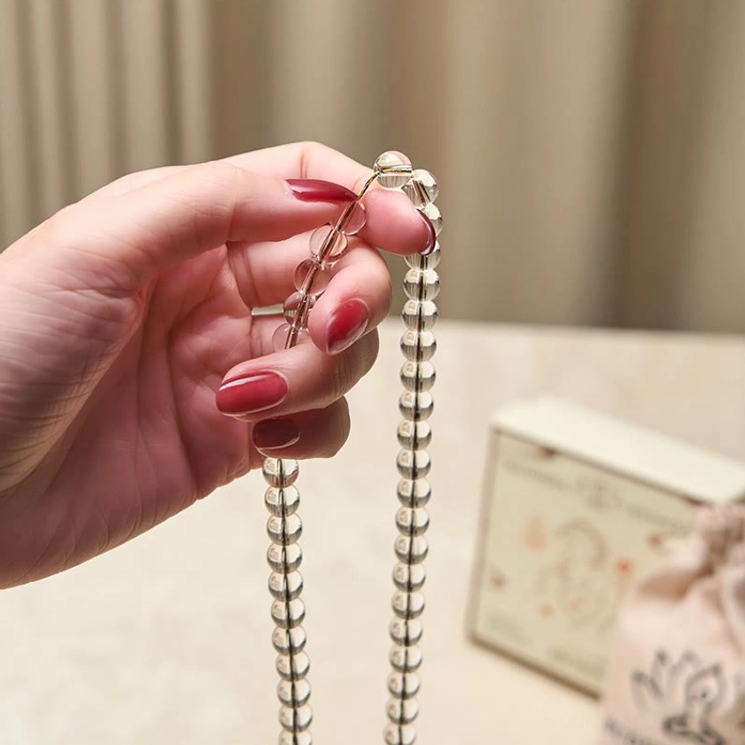 Buddhist mala with clear crystal beads and silver vajra charm - close-up detail of metal tassel and bead clasp held between fingers