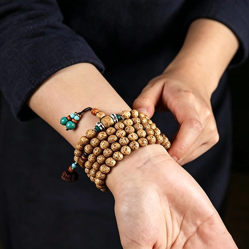 Hands adjusting stacked Star Moon Bodhi Seed mala wrap bracelets with decorative tassels close-up action shot