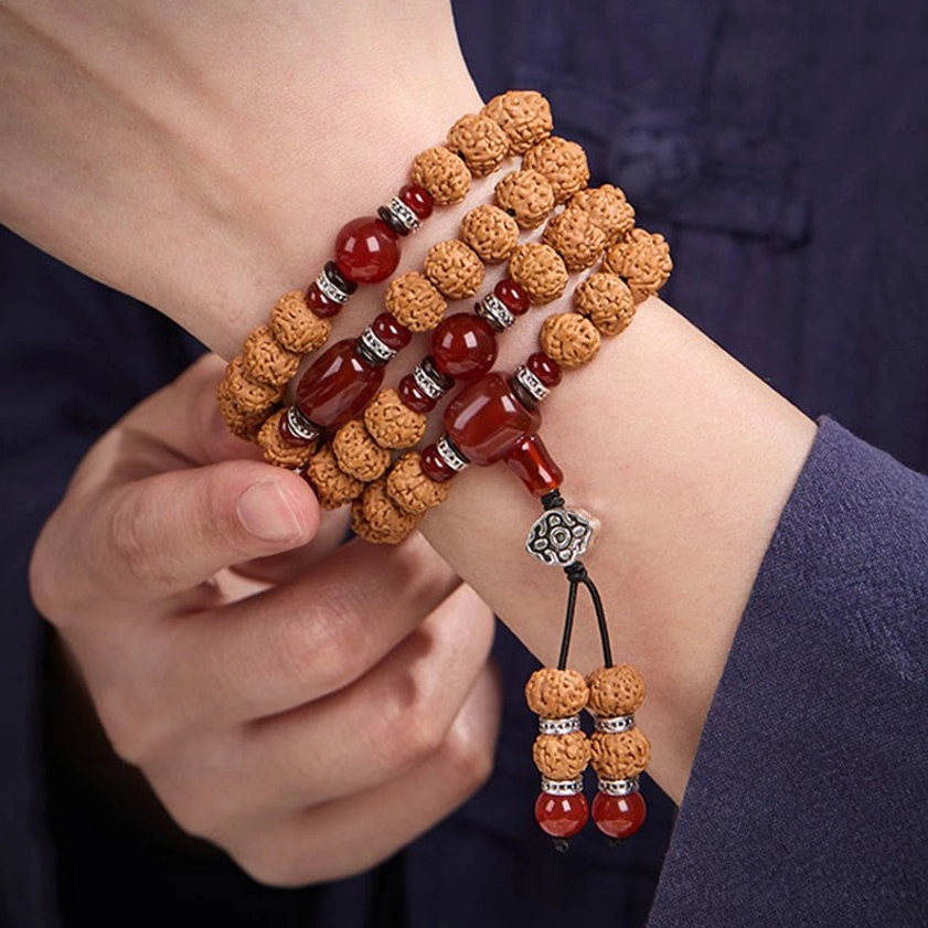 Close-up of prayer mala worn on wrist with three-eye dzi bead and decorative tassel pendant detail