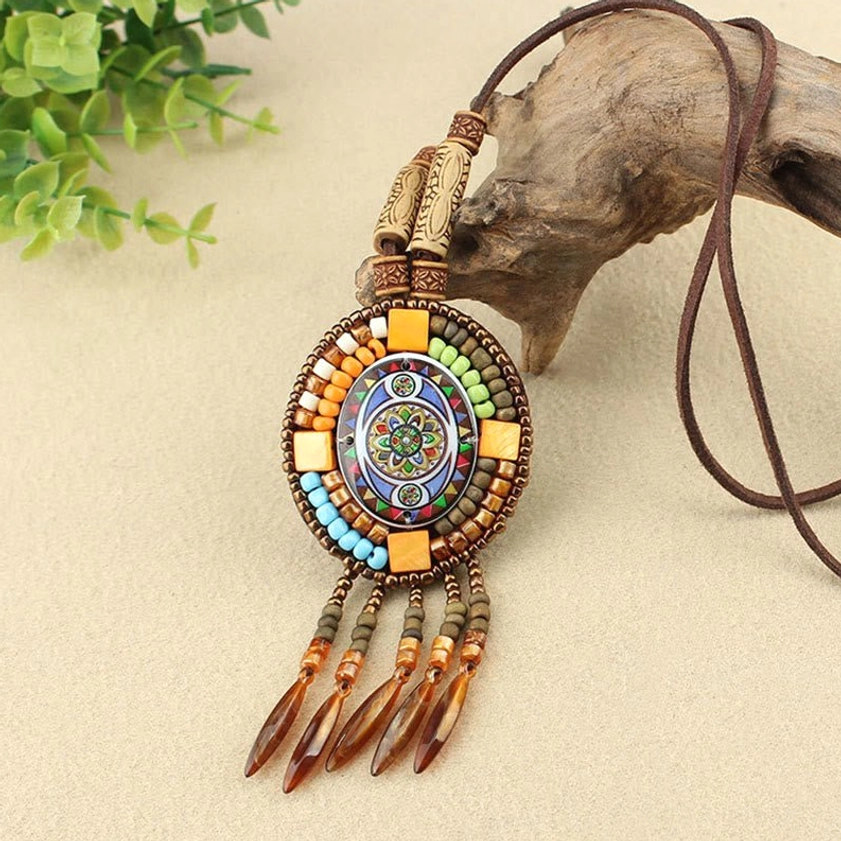 Round mandala mosaic pendant necklace with wooden beads and tassel details on driftwood backdrop with greenery