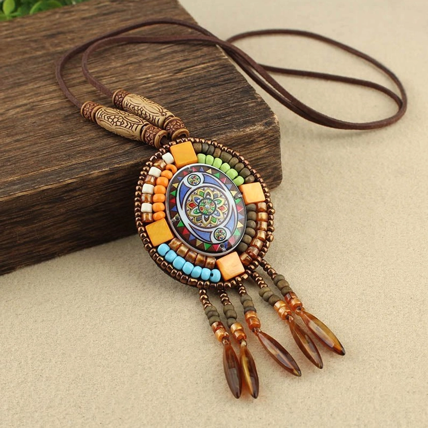 Colorful mosaic mandala pendant necklace with brown tassel charms and wooden accents on dark wood block