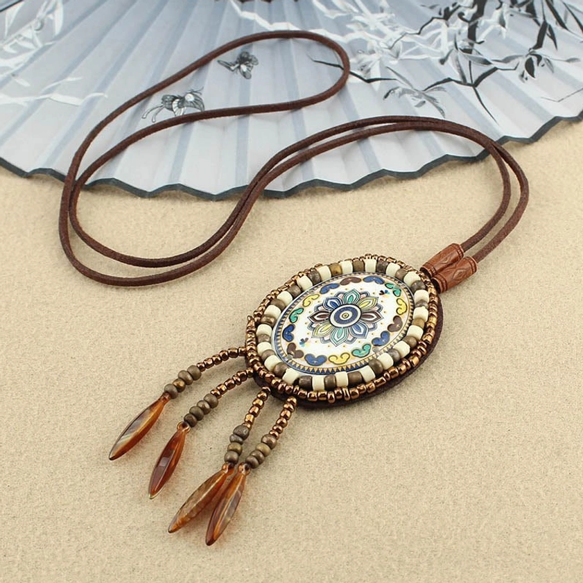Neutral tone mandala pendant necklace with brown tassel charms and genuine leather cord on beige background