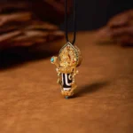 Manjusri Bodhisattva Dzi Bead Pendant Necklace with hand-painted two-eye dzi bead and gilded copper setting, front three-quarter view on wooden studio background
