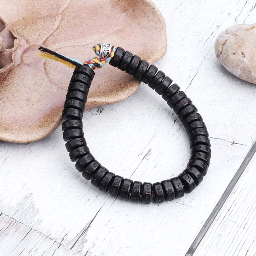Handmade sacred mantra bracelet on wooden surface with natural stones, showing colorful tassel closure and engraved beads