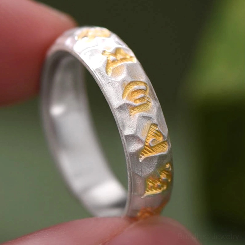 Mantra ring close-up on fingertip showing detailed hammered texture and intricate gold Sanskrit engravings