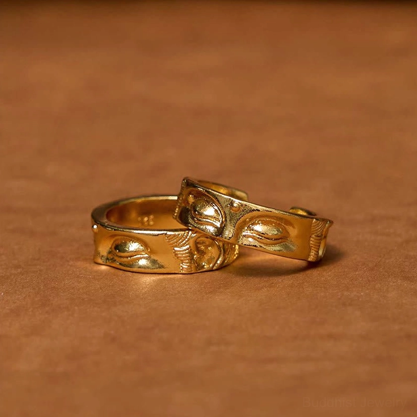 Two matching Buddha meditation copper rings with polished golden finish and embossed Buddhist eye motifs on brown leather surface