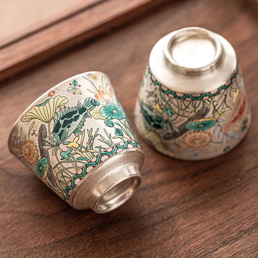 Pair of matching ceramic tea cups with fish and lotus design, silver rim, top-down view