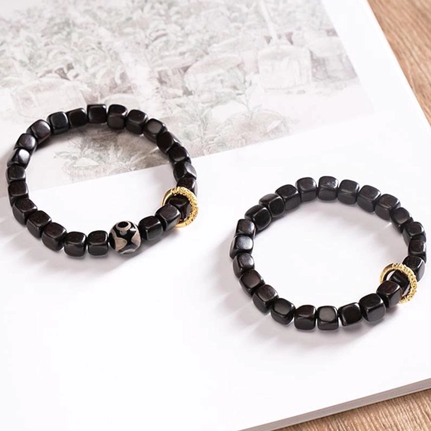 Pair of matching ebony wood dzi bead bracelets displayed on white paper, one with nine-eye dzi bead and copper ring, one plain cubic bead style