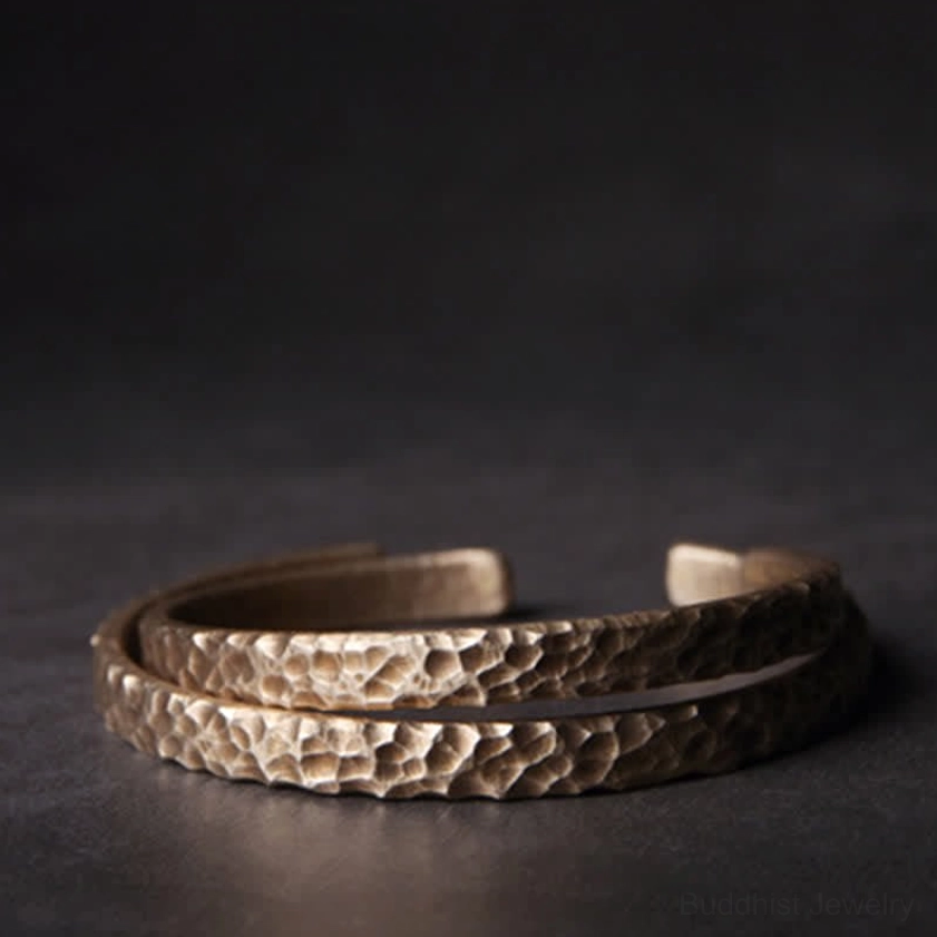 Pair of matching hammered copper open cuff bracelets stacked together on dark studio background
