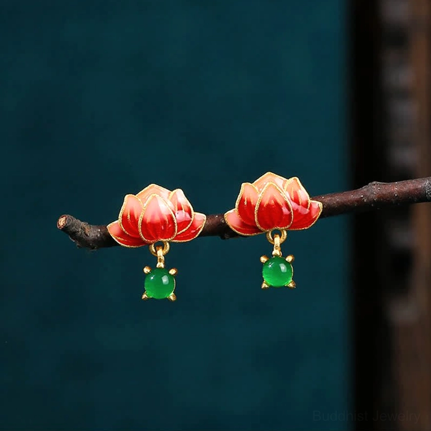 Pair of matching red lotus drop earrings displayed on dark wooden branch against teal background, low side angle view
