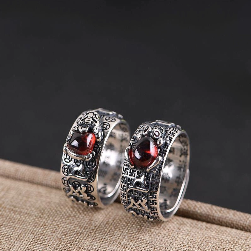 Two matching Buddhist wealth rings with Pixiu engravings and red gem settings, flat lay on linen fabric