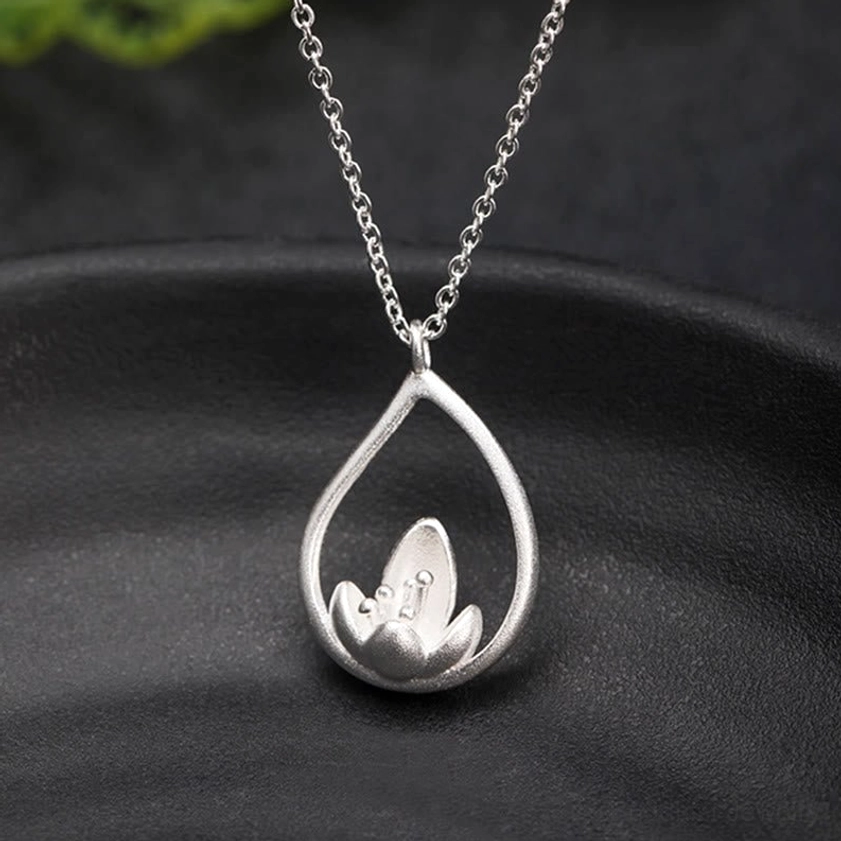 Matte finish sterling silver lotus pendant necklace, front eye-level view clearly showing teardrop frame and intricate lotus decoration with green foliage accent