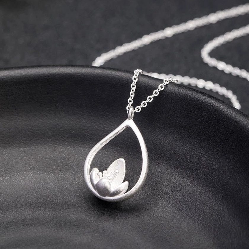 Silver lotus flower necklace resting on dark ceramic dish, side view highlighting twisted cable chain and polished lotus pendant surface