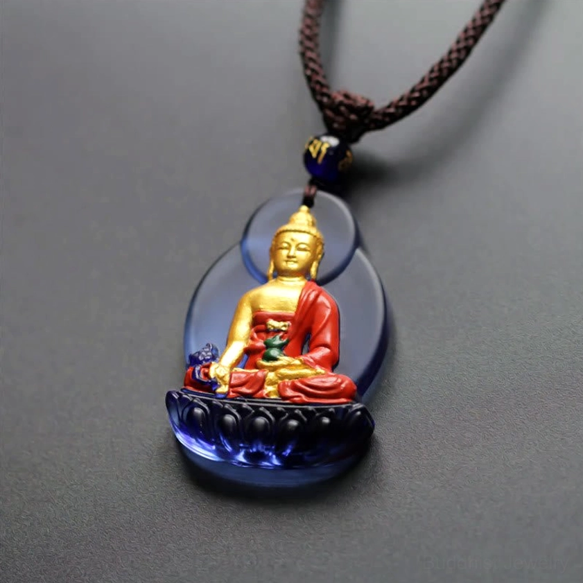 Compact Medicine Buddha crystal pendant in brown braided cord, top-down view showing intricate hand-painted details