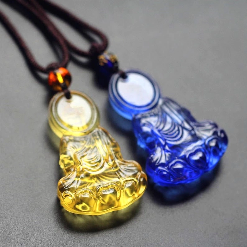 Two mixed Liuli crystal Medicine Buddha pendants in yellow and royal blue translucent glass on decorative brown cords, flat lay collection display